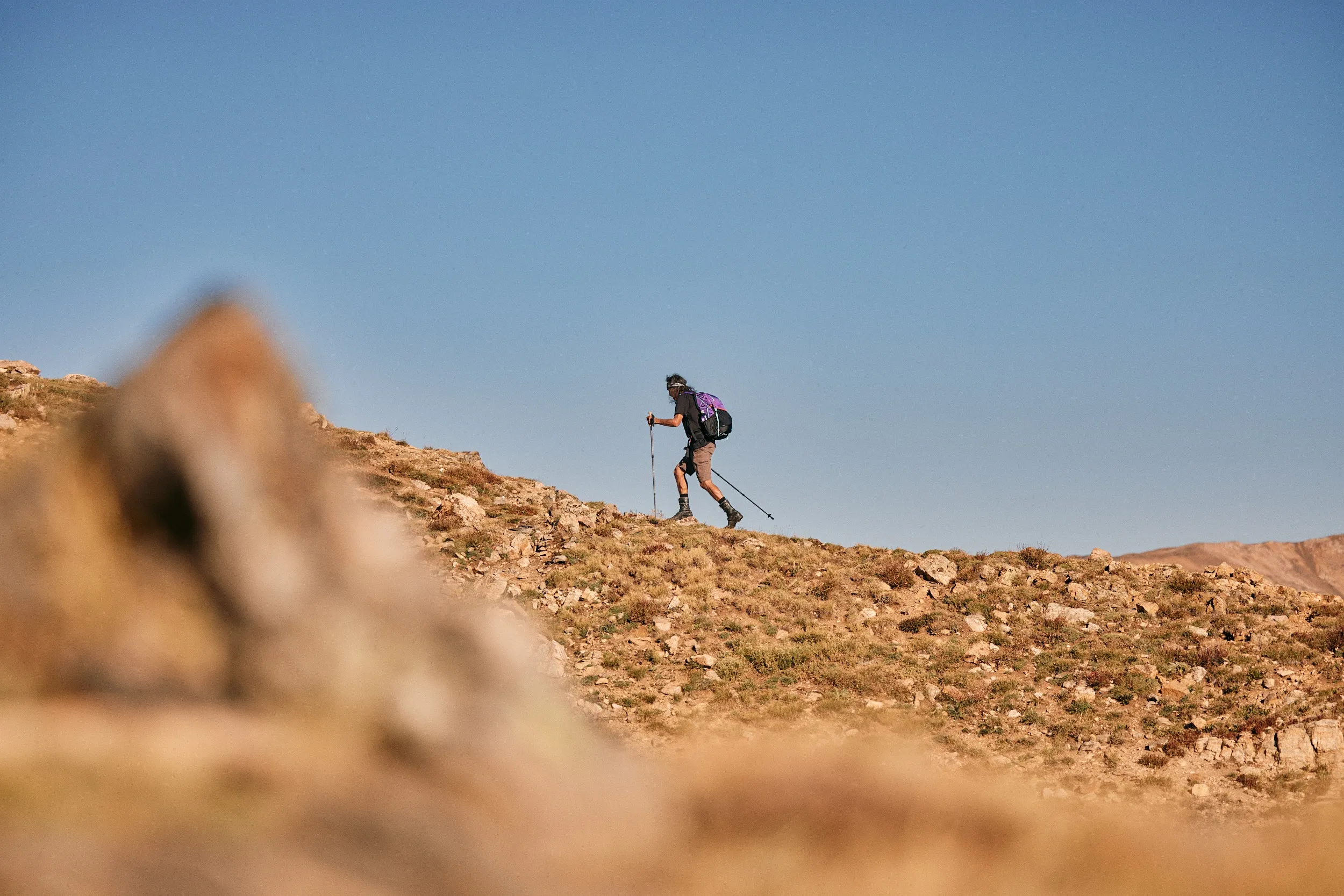 Hiker with a purple Gossamer Gear pack climbing a rocky alpine ridge
