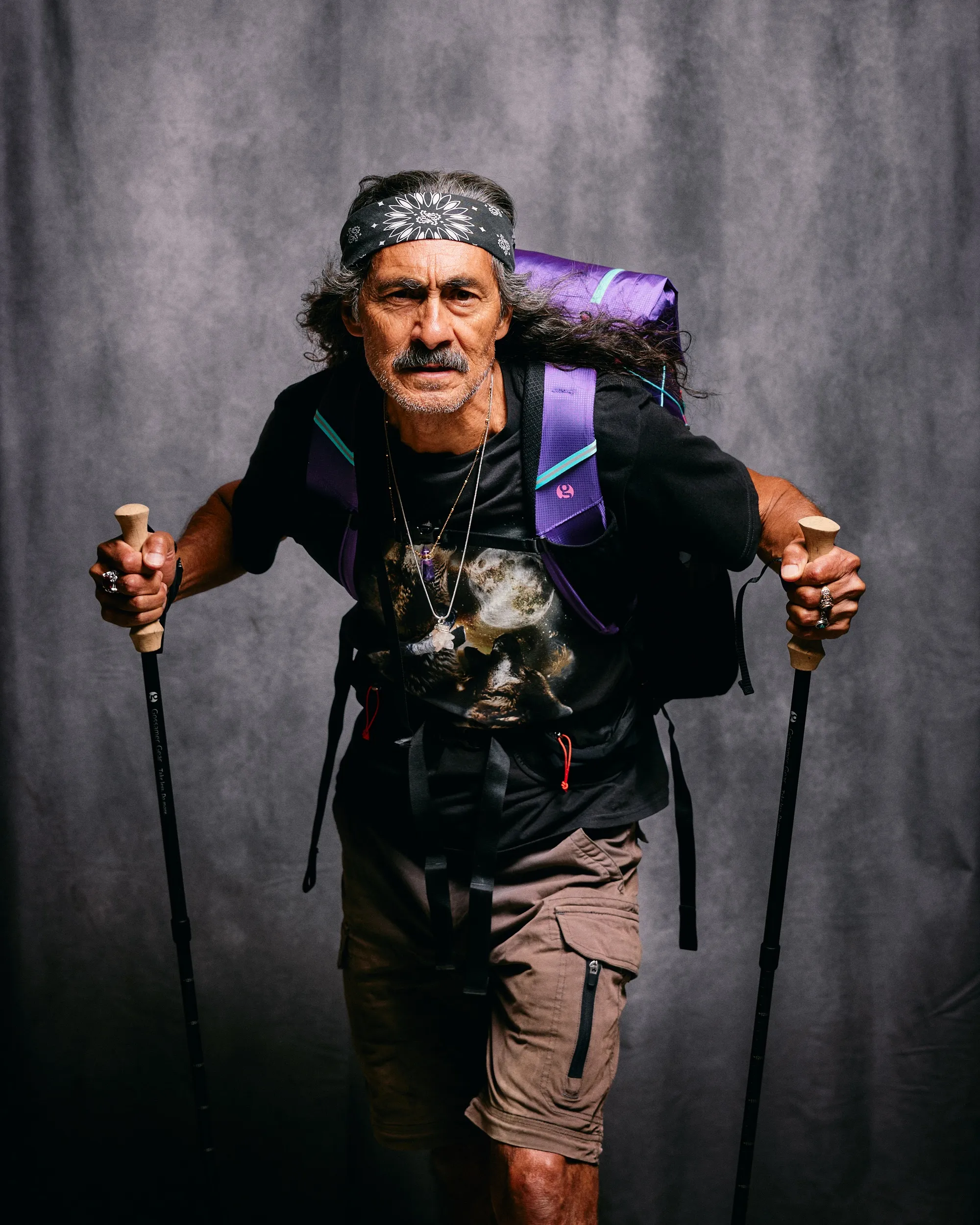 Studio portrait of a hiker in a bandana holding trekking poles, purple pack on